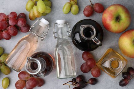 Different types of vinegar and fresh fruits on grey table, flat lay
