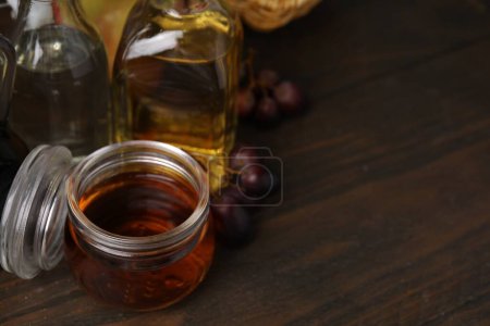 Different types of vinegar and grapes on wooden table, space for text