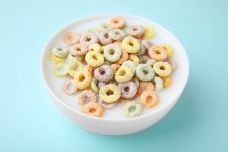 Photo for Tasty colorful cereal rings and milk in bowl on turquoise background - Royalty Free Image