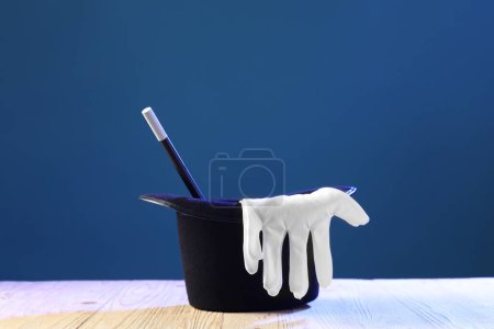 Magician's hat, wand and gloves on wooden table against blue background