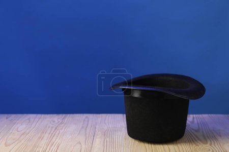 Sombrero de mago sobre mesa de madera sobre fondo azul, espacio para texto