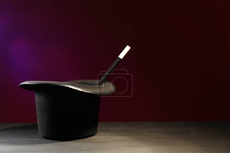 Zauberhut und Zauberstab auf schwarzem Holztisch vor dunklem Hintergrund, Platz für Text