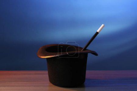 Magician's hat and wand on wooden table against blue background