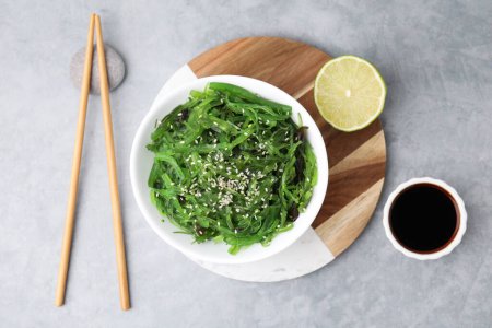 Tasty seaweed salad in bowl served on gray table, flat lay