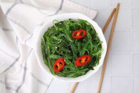 Tasty seaweed salad served in bowl on white tiled table, top view