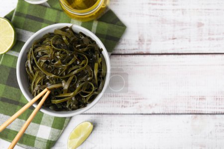 Tasty seaweed salad in bowl served on wooden table, flat lay. Space for text