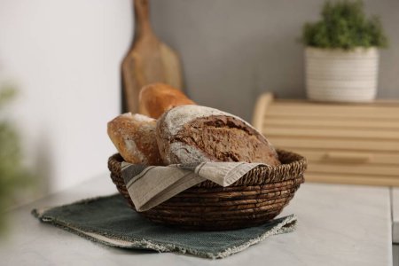 Cesta de pan de mimbre con panes recién horneados sobre mesa de mármol blanco en la cocina