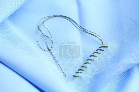 Téléchargez les photos : Aiguille à coudre avec fil et points sur tissu bleu clair, vue du dessus - en image libre de droit