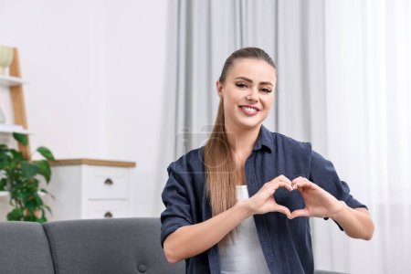 Glückliche Frau zeigt Herz-Geste mit Händen zu Hause, Raum für Text