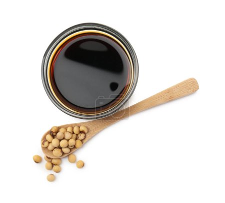 Tasty soy sauce in bowl, soybeans and spoon isolated on white, top view