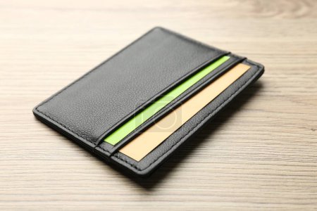 Leather business card holder with colorful cards on wooden table, closeup