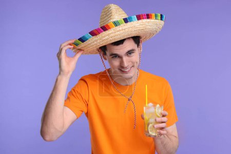 Joven en sombrero mexicano con cóctel sobre fondo violeta