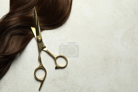 Tijeras de peluquería profesional con hebra de pelo castaño sobre mesa gris, vista superior. Espacio para texto