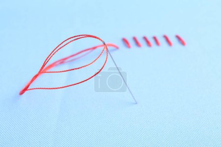 Sewing needle with thread and stitches on light blue cloth, closeup