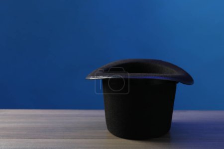Sombrero de mago sobre mesa de madera sobre fondo azul, espacio para texto