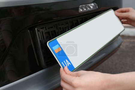 Woman installing vehicle registration plate outdoors, closeup