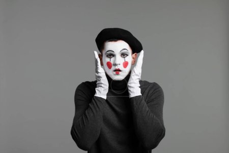 Mime-Künstler in Baskenmütze posiert auf grauem Hintergrund
