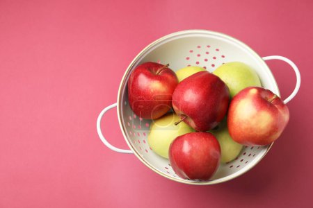 Colander with fresh apples on pink table, top view. Space for text