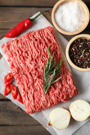 Photo for Raw ground meat, spices, rosemary and onion on wooden table, flat lay - Royalty Free Image
