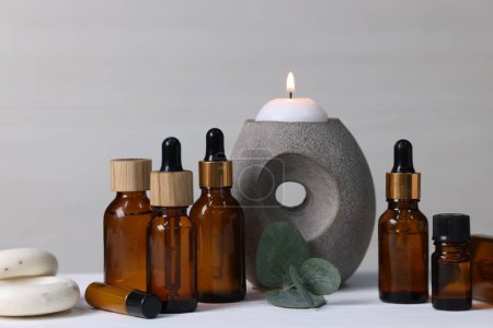 Verschiedene Aromatherapie-Produkte, brennende Kerzen und Eukalyptusblätter auf weißem Holztisch