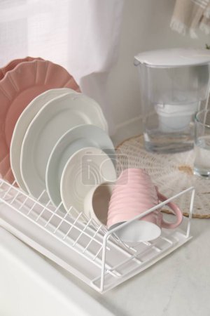Drainer with different clean dishware and cup on light table indoors