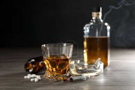 Téléchargez les photos : Alcool et toxicomanie. Whisky en verre, seringue, pilules et cigarettes sur table en bois - en image libre de droit