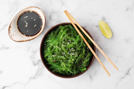 Tasty seaweed salad in bowl served on white marble table, flat lay