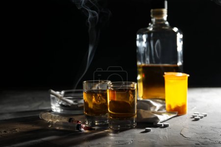 Téléchargez les photos : Alcool et toxicomanie. Whisky dans les verres, seringues, pilules et cocaïne sur table grise - en image libre de droit