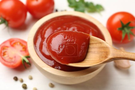 Photo for Taking delicious tomato ketchup with spoon from bowl at white table, closeup - Royalty Free Image