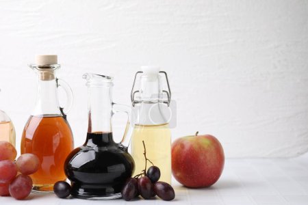 Different types of vinegar and ingredients on light tiled table, closeup. Space for text