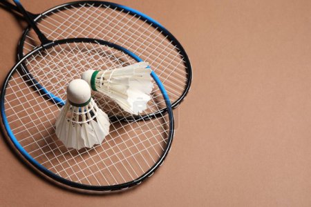 Photo for Feather badminton shuttlecocks and rackets on brown background, space for text - Royalty Free Image