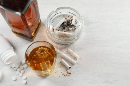 Alcohol y drogadicción. Whisky en vidrio, cigarrillos y pastillas en la mesa blanca, por encima de la vista. Espacio para texto