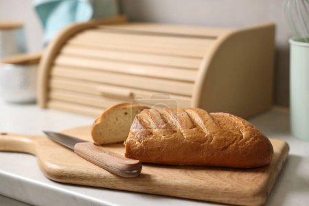 Wooden bread basket, freshly baked loaf on white marble table in kitchen