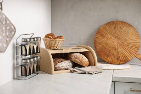 Wooden bread basket, freshly baked loaves and croissants on white marble table in kitchen