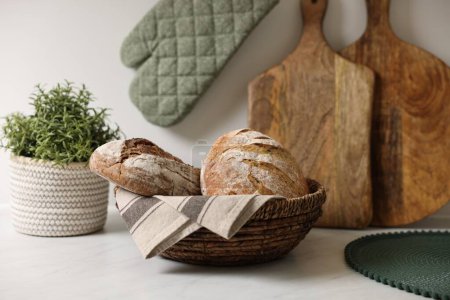 Cesta de pan de mimbre con panes recién horneados sobre mesa de mármol blanco en la cocina