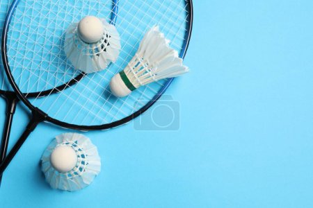 Photo for Feather badminton shuttlecocks and rackets on light blue background, flat lay. Space for text - Royalty Free Image