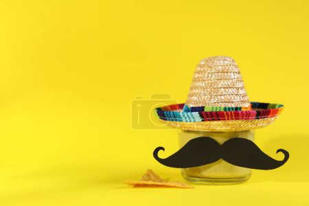 Téléchargez les photos : Délicieux guacamole, puce de nachos, chapeau de sombrero mexicain et fausse moustache sur fond jaune. Espace pour le texte - en image libre de droit