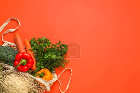String bag with fresh vegetables and herbs on coral background, top view. Space for text