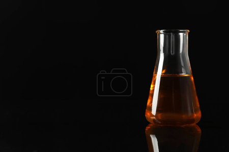Photo for Glass flask with yellow oil on black background, space for text - Royalty Free Image