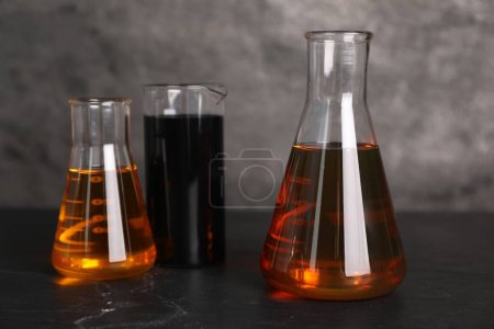Bécher et flacons avec différents types d'huile sur table grise texturée