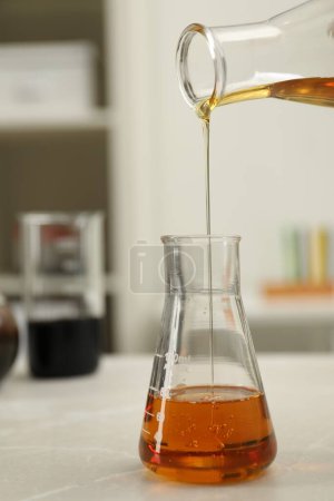 Téléchargez les photos : Verser du pétrole brut orange dans une fiole à table en marbre clair, gros plan - en image libre de droit