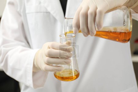 Laborangestellte gießt orangefarbenes Rohöl in Kolben, Nahaufnahme