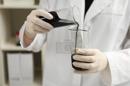 Photo for Laboratory worker pouring black crude oil into flask indoors, closeup - Royalty Free Image