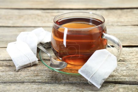 Thé aromatique dans une tasse en verre, cuillère et sachets de thé sur une table en bois