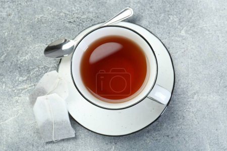 Aromatic tea in cup, teabags and spoon on grey table, top view
