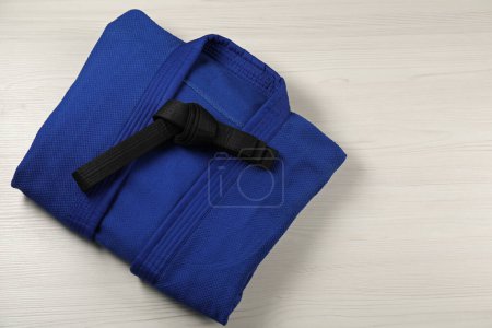 Black karate belt and blue kimono on wooden background, top view. Space for text