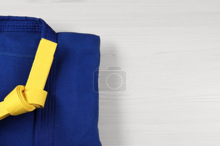 Yellow karate belt and blue kimono on wooden background, top view. Space for text