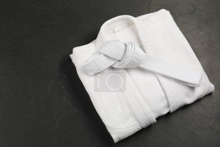 White karate belt and kimono on gray background, top view. Space for text