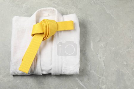 Yellow karate belt and white kimono on gray marble background, top view. Space for text