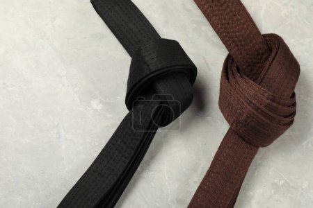 Photo for Black and brown karate belts on gray marble background, flat lay. Space for text - Royalty Free Image